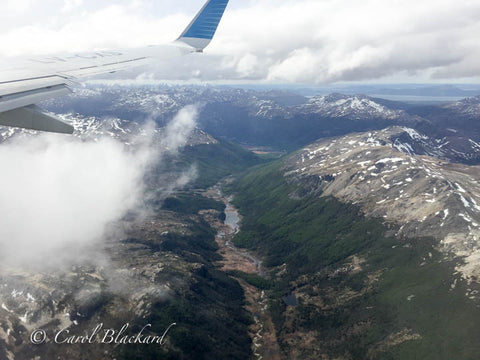 View from airplane window of rugged terrain, snow, river