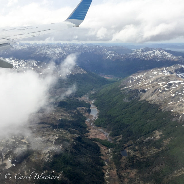 View from airplane window of rugged terrain, snow, river